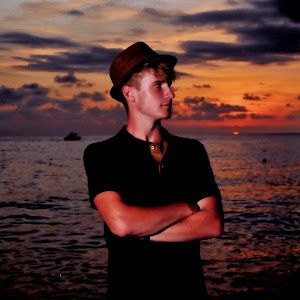 Nico Gleichmann mit Hut und verschränkten Armen vor einem Sonnenuntergang am Meer